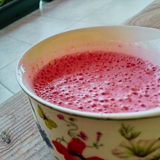 Céklás eper turmix virágmintás csészében, frissítő nyári ital habos, rózsaszín felszínnel, fa asztalon tálalva.