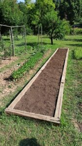 Emelt ágyás fából készült kerettel, friss földdel és komposzttal feltöltve a kertben.