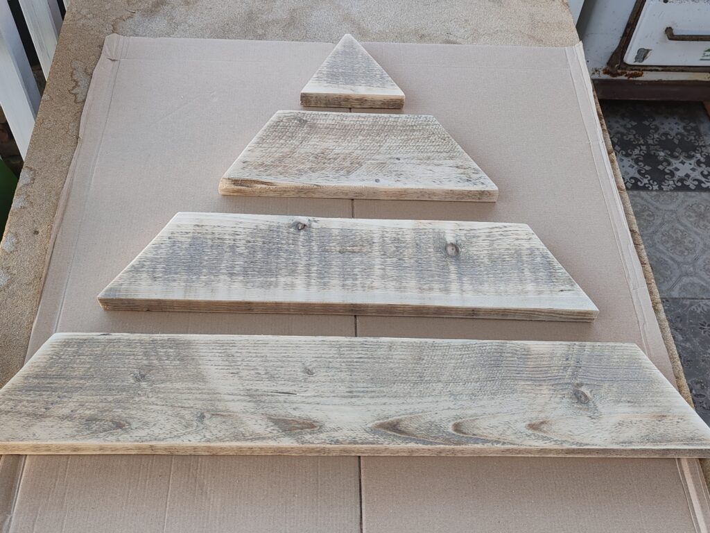 Csiszolt, méretre vágott deszkák karácsonyfa formába rendezve egy asztalon, festésre és összeállításra előkészítve.