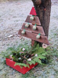 Madárbarát kültéri karácsonyfa piros ládában, fenyőágakkal, tobozokkal és házi készítésű madáreleség díszekkel, fagyos téli kertben.