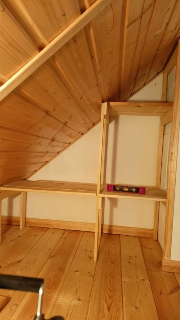 Szellős tetőtéri polc kialakítása ferde fal mellett, szerelés közben