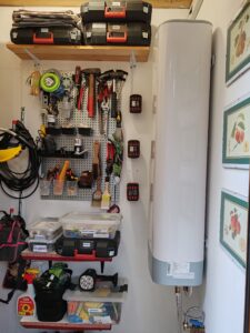 Fali szerszámtároló pegboarddal, polcokkal és dobozokkal egy kis helyiségben, a kazán mellett kialakítva